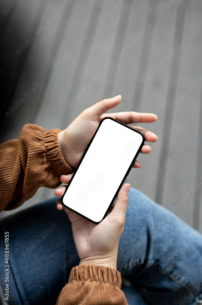 Wall mural close-up image of a woman in casual clothes sitting outdoors in the city and using her smartphone.