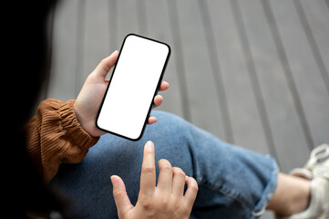 Close-up image of a woman using her smartphone while sitting outdoors street.