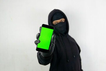 Masked thief holding smartphone mockup of blank screen. green screen smart phone for mock up