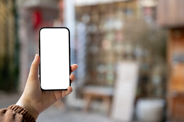 A woman's hand holding a smartphone mockup over a blurred background of a retail shop on the street.