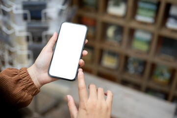 A smartphone mockup in a woman's hand with a blurred background of a retail shop on the street.