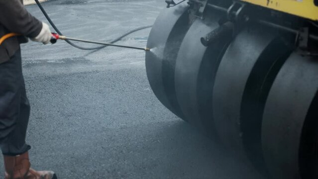 Water spraying on pneumatic tyred roller. Process asphalting road construction infrastructure by compressing, compacting, leveling and smoothing the asphalt road surface using a pneumatic tyred roller