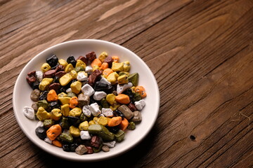 chocolate pebbles in a small ceramic dish. Chocolate candy in the form of small colorful pebbles. on wooden table. Coklat kerikil. 