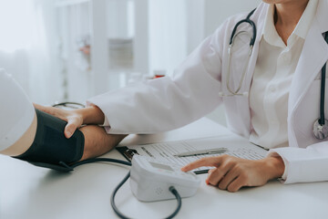 Female doctor's hands using a blood pressure monitor and stethoscope to check blood pressure on a...