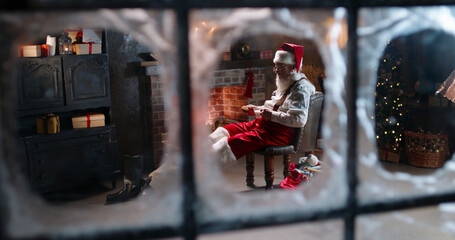 Tired Santa Claus sleeping near fireplace, holding cookies and cup with milk outside view through window. Overworked Mr Claus relaxing, sitting with legs outstretched. House of Santa, free time.