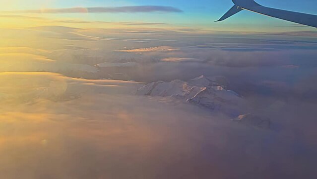 View from the airplane window to sunset, clouds, mountains.