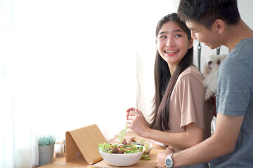 Happy cheerful Asian young couple preparing a vegetable salad in kitchen together in weekend.