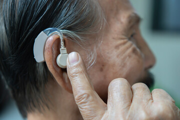 Close up shot of elder patient wear audiphone to improve his hearing and pointing on hearing aid...