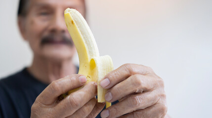 Close-up of an elderly Asian man's hand. He's preparing a banana for eating.