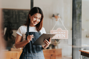 Happy excited attractive young Asian woman in denim apron, received online order in coffee shop...