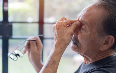 Side view of mature old Asian man rubbing and wiping eyes and takes off glasses, feels eyes pain,...
