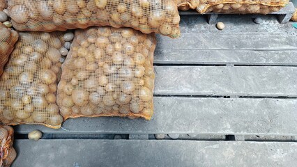 The portrait of a stack of potato seeds inside an orange sack on top of a wooden pallet
