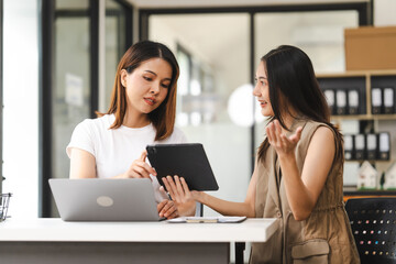 Two Asian colleagues, freelance writer and graphic designer discussing about creating characters in screenplays work and smiling with tablets and a laptop, journalist, artist, meeting together