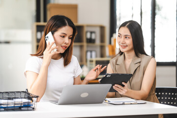 Two Asian colleagues, freelance writer and graphic designer discussing about creating characters in screenplays work and smiling with tablets and a laptop, journalist, artist, meeting together