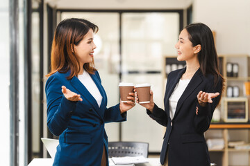 Two middle aged and young Asian female executives in formal suits review bar chart, discussing business strategies in office setting, senior executives or directors in advertising or public relations