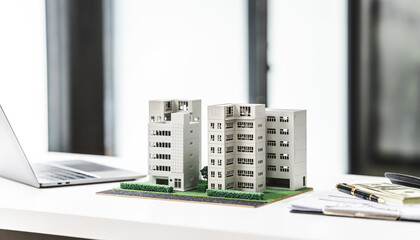 Model buildings on a desk next to a laptop, symbolizing city real estate investing and large...