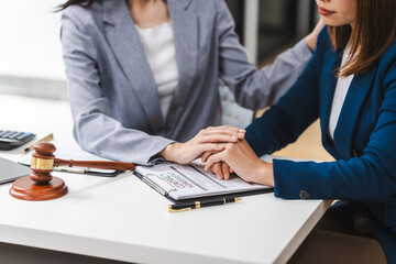 Two middle aged and young Asian lawyer in a formal suit consoles a client during a legal consultation, with a gavel and documents on the table.