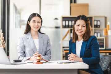 Two middle aged and young Asian lawyer in a formal suit consoles a client during a legal consultation, with a gavel and documents on the table.
