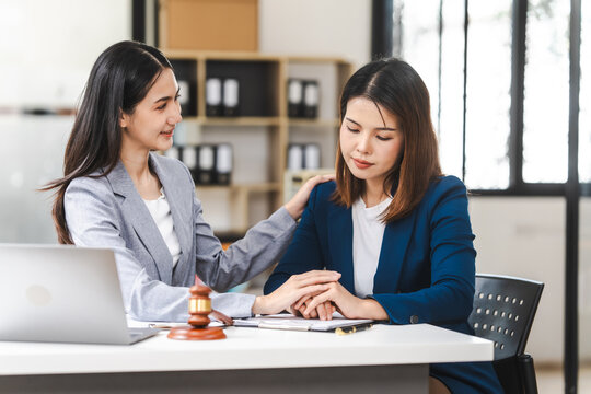 Two middle aged and young Asian lawyer in a formal suit consoles a client during a legal consultation, with a gavel and documents on the table.