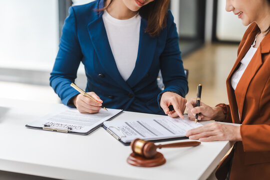 Two young and middle-aged Asian women lawyers in formal suits discuss legal contract, focusing on legislation and women's rights in law office.