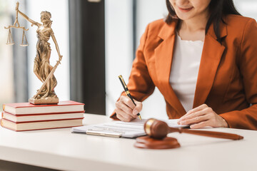 Young attractive Asian female lawyer in formal suit works on tablet with laptop, legal books, and...