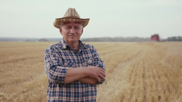 Happy adult farmer stands and smile at the camera against background of working tractor in field. Concept ecology, transport, outdoor nature, clean air, food. Natural production bio product.