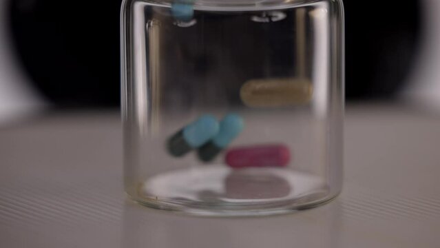 Pharna pills falls into glass jar filmed in slow motion - close up shot - various tablets