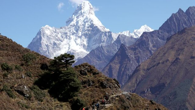 Trekking to Everest Base Camp. Tourists with backpacks are walking along footpaths trail on hilly rocky of Himalayan mountains. Hiking in Nepal with snow capped peaks against Ama Dablam