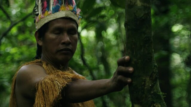 Portrait of an indigenous guy wearing a feathered hat and fringed shirt in the dense forest in Leticia, Amazon, Colombia