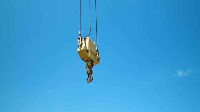 Witness the ramshorn hook of a crane suspended in the sky. The camera circles, unveiling the enormity of a giant marine crane