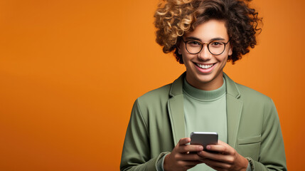 Fototapeta premium Young man holding mobile phone and smiling on solid orange background