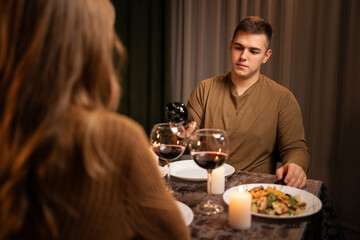 Cheerful couple drinking wine and having romantic dinner with candlelight in the evening at home. Date night, clinking wineglasses.