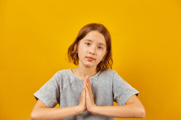 Pleading teen girl on yellow studio background