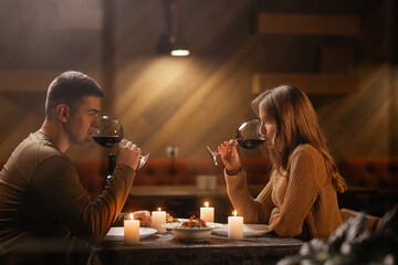 Young love couple clinking glasses at Valentine's day dinner in restaurant sitting near window