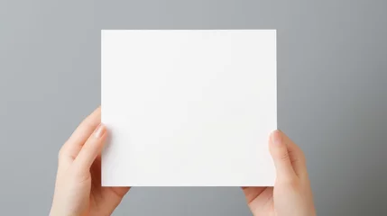 Fotobehang Blank white square greeting card opened by female hand with manicured nails. Mockup. Top view. Stylish and blurry background. For the text entry area © ND STOCK