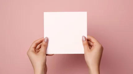 Fotobehang Blank white square greeting card opened by female hand with manicured nails. Mockup. Top view. Stylish and blurry background. For the text entry area © ND STOCK
