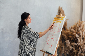 A woman artist paints a picture on an easel in an art studio