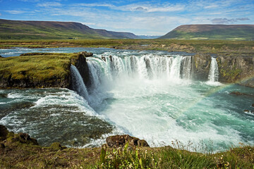 The Skjalfandafljot river crashes over the Godafoss Waterfall in Northern Iceland with a partly cloudy sky in the background