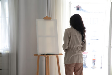 Fototapeta na wymiar A woman artist at an easel in an art studio paints a picture