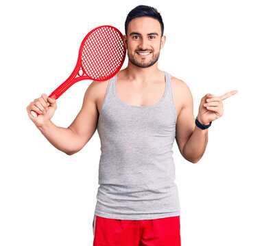 Young handsome man holding tennis racket smiling happy pointing with hand and finger to the side