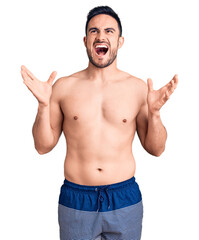Young handsome man wearing swimwear crazy and mad shouting and yelling with aggressive expression...