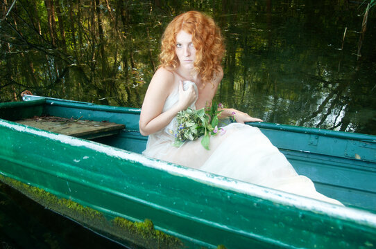 Nice young lovely shy reserved girl, sensual seductive young sexy woman, redhead with red hair, sitting naked covered with white cloth in the green boat on the lake