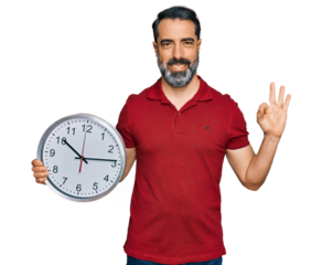 Middle aged man with beard holding big clock doing ok sign with fingers, smiling friendly gesturing excellent symbol