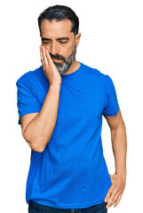 Middle aged man with beard wearing casual blue t shirt thinking looking tired and bored with depression problems with crossed arms.
