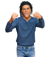 Fototapeta premium Young african american man wearing casual winter sweater angry and mad raising fists frustrated and furious while shouting with anger. rage and aggressive concept.