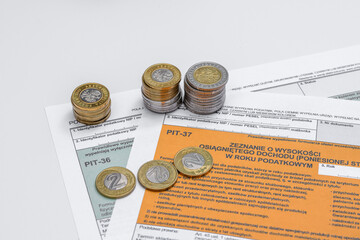 Polskie monety poukładane w stosu leżą na formularzu zeznania podatkowego pit37
