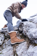  Adult Woman Climbing Over a Rock in Mountains in Vintage Mountain Clothes from Low Angle View...