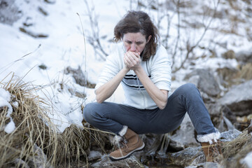 Caucasian Woman Hiker Blows into Hands, Warming Up after Washing in Icy Alpine Stream. Winter Wilderness Adventure