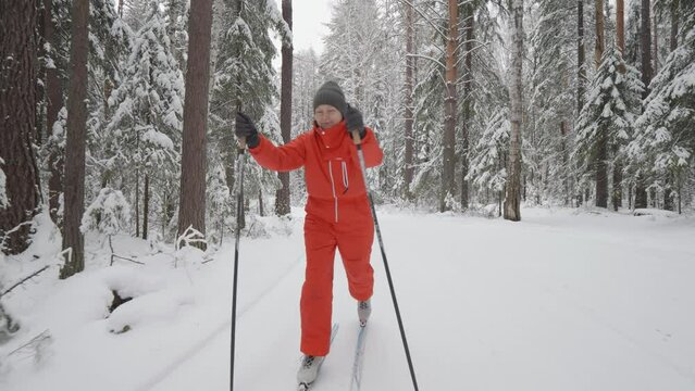 Woman in red sport clothes enjoys cross-country skiing in beautiful snowy winter forest.
