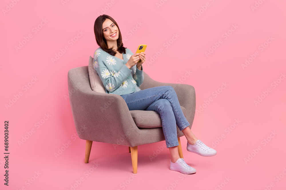 Sticker Full length photo of attractive young woman using her new apple smartphone sit comfortable chair waiting room isolated on pink background